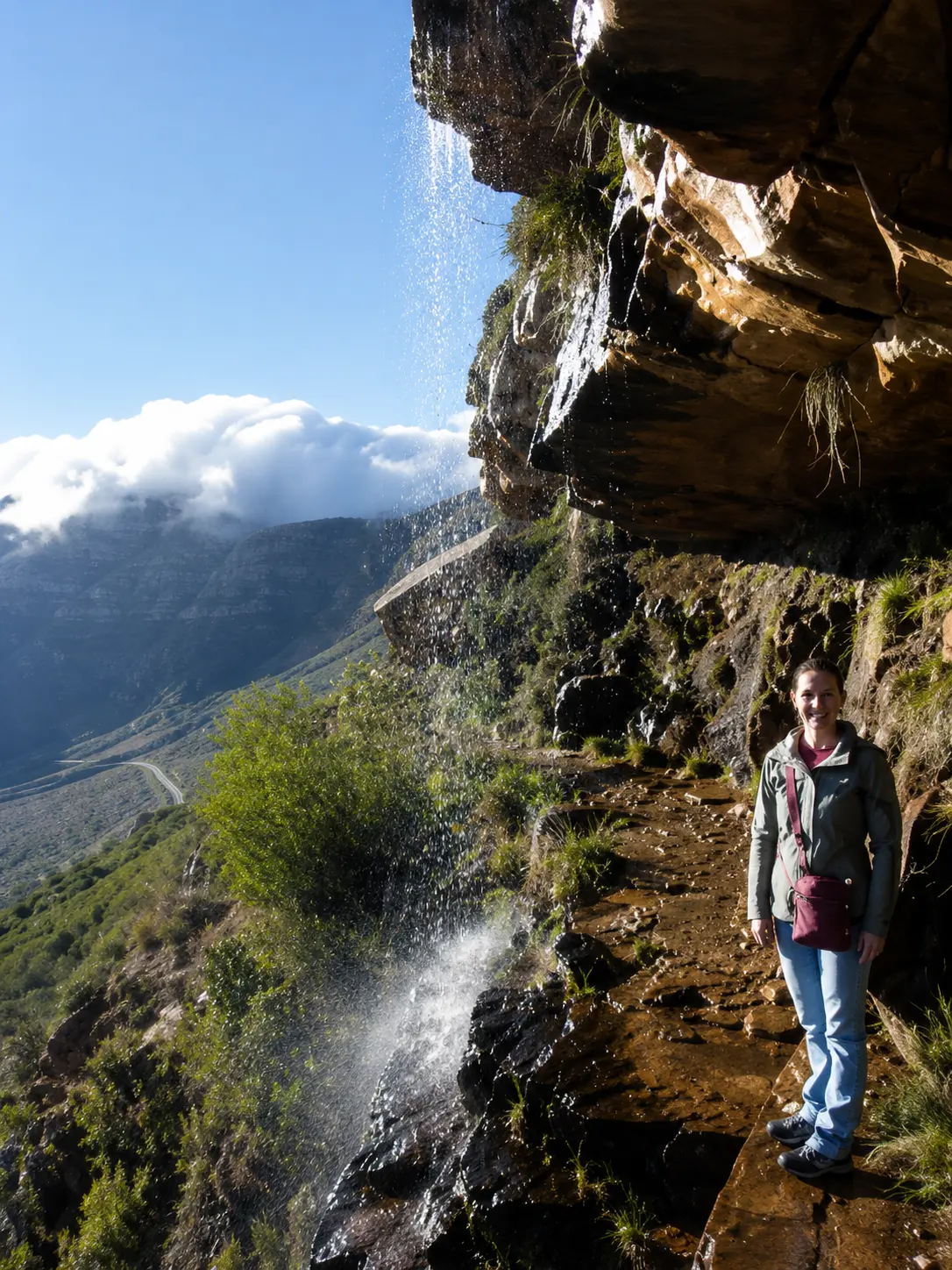 Hiker standing beside a small waterfall cascading over rocky cliffs along a Table Mountain hiking trail in Cape Town.