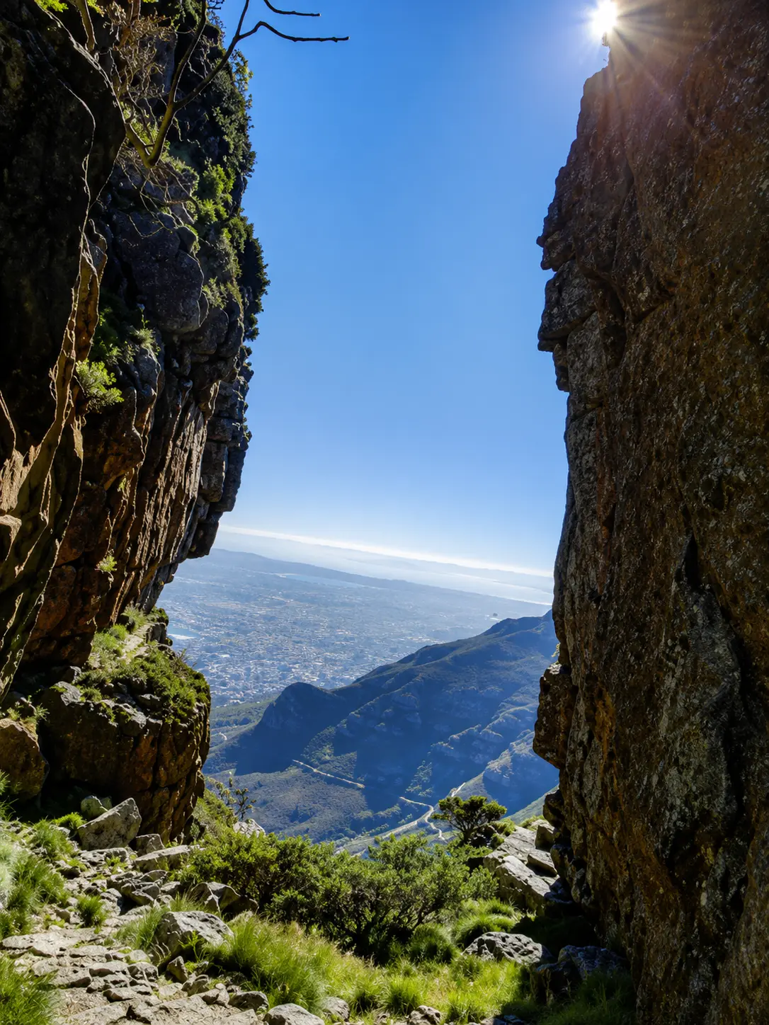 View through a dramatic rocky gorge on Table Mountain overlooking Cape Town, surrounding mountains.