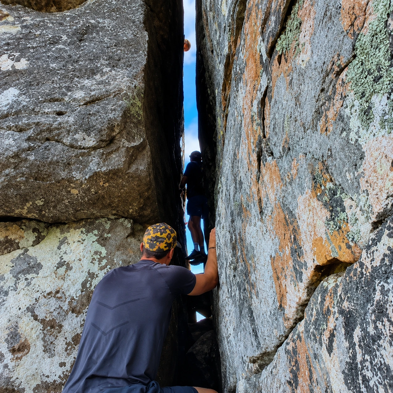 Hikers climbing through a narrow passage between massive sandstone rocks on an adventurous Table Mountain route in Cape Town.